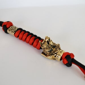 May include: A red and black paracord keychain with a wolf head charm. The charm is made of metal and has the inscription "IAY HA" on the side.