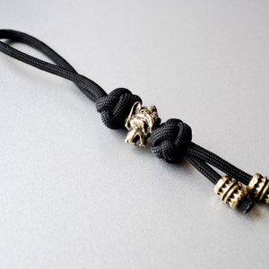 May include: Black paracord keychain with a gold metal wolf head charm and two gold metal beads.