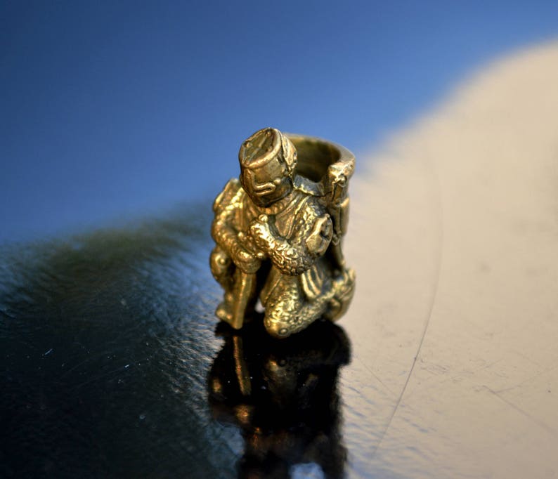 以下が含まれることがあります： 鎧を着たひざまずく騎士の金色の金属製フィギュア。フィギュアは細部まで作り込まれており、リアルな外観をしています。