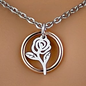 May include: Silver-tone necklace with a rose pendant. The pendant features a white rose design within a gold-tone circle. The necklace chain is a silver-tone cable chain.