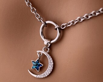 Puede incluir: Un collar de cadena de plata con un colgante de luna creciente y un dije de estrella azul. El colgante está adornado con pequeños cristales transparentes.
