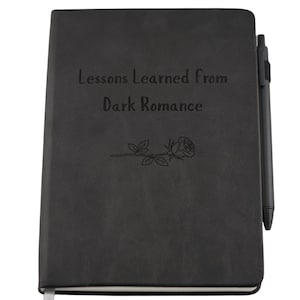 May include: A black journal with the text "Lessons Learned from Dark Romance" and a rose illustration. A black pen is attached to the side. The journal has a ribbon bookmark.