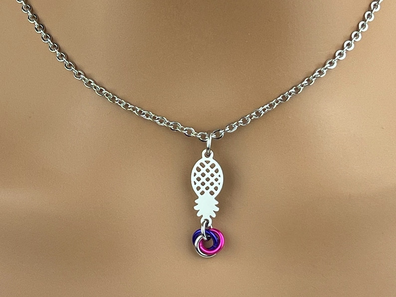 Puede incluir: Un collar de cadena de plata con un colgante de pi&ntilde;a y un charm de anillo tricolor en rosa, azul y morado.