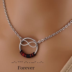 May include: Silver-toned necklace with a circular pendant featuring an infinity symbol and wrapped with red and black thread. The word "Forever" is below the pendant in a simple font.