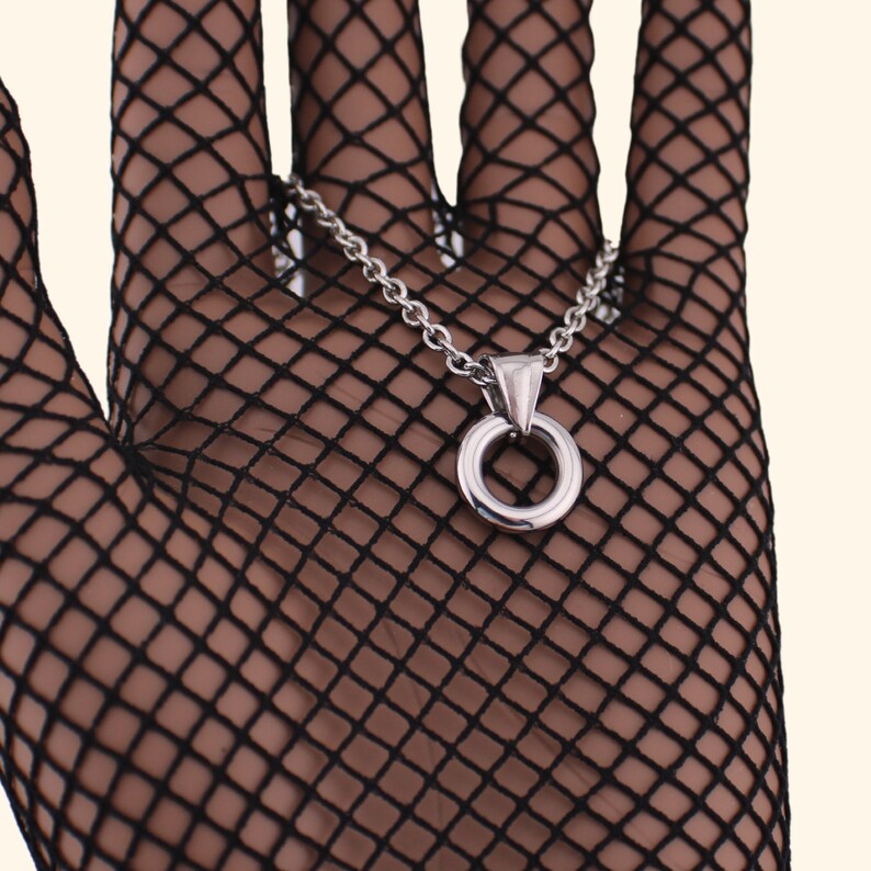 Peut inclure: Un collier en cha&icirc;ne argent avec un pendentif rond simple. Le collier est pr&eacute;sent&eacute; sur un gant en r&eacute;sille noir.