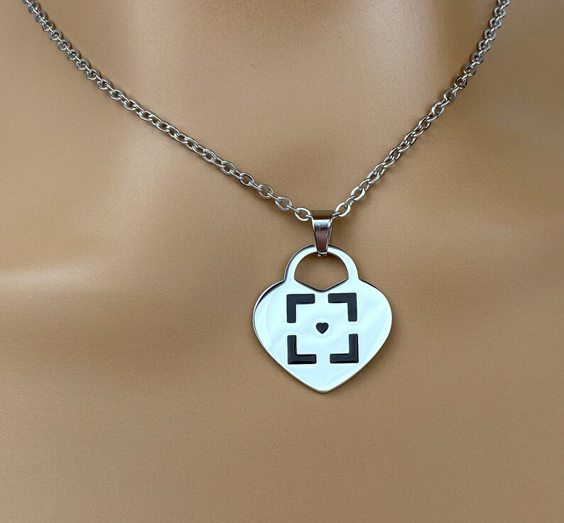 May include: A silver necklace with a heart-shaped pendant featuring a black square with a small heart in the center.
