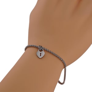 Peut inclure: Un bracelet argenté avec un pendentif en forme de cadenas en cœur. Le pendentif comporte un trou de serrure. Le bracelet est de type chaîne. Le bracelet est porté au poignet.