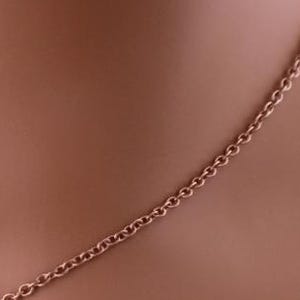 May include: A close-up of a rose gold chain necklace. The chain is made of small, interlocking oval links. The necklace is displayed on a mannequin.