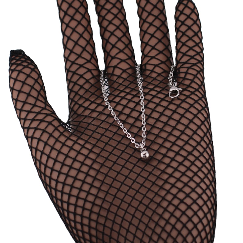 May include: A silver chain necklace with a small silver ball pendant. The necklace is displayed on a black fishnet glove.