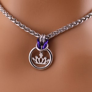 May include: A silver chain necklace with a purple accent and a pendant featuring a crown inside a circle.