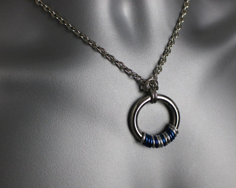May include: A silver chain necklace with a silver ring pendant. The ring is decorated with blue rings.