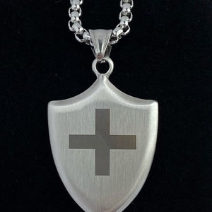 May include: A silver chain necklace with a silver shield pendant featuring a cross design.