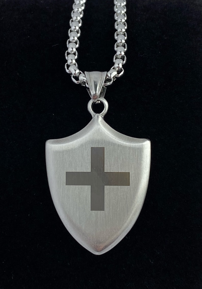 May include: A silver chain necklace with a silver shield pendant featuring a cross design.