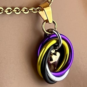May include: A gold chain necklace with a pendant featuring a heart-shaped charm surrounded by interlocking rings in purple, yellow, black, and white.