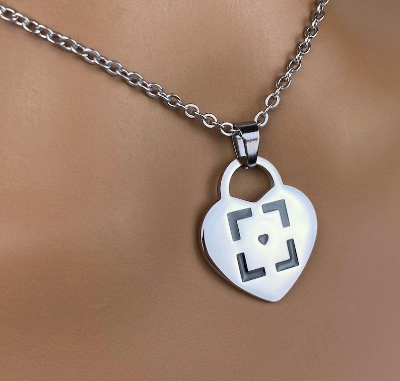 May include: A silver heart-shaped pendant necklace with a black square design and a small heart in the center.