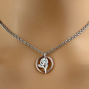 May include: A silver-toned necklace with a delicate rose pendant. The pendant features a white rose design within a gold-colored circle. The chain is a simple, elegant design.