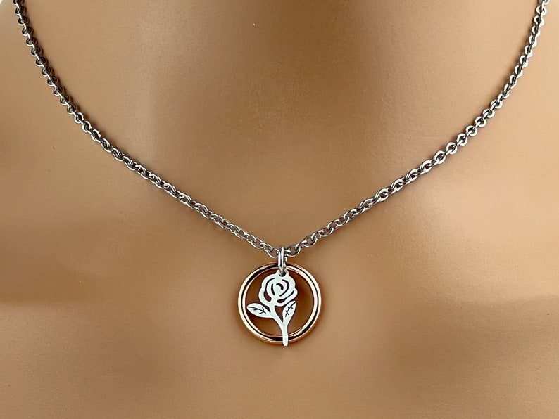 May include: A silver-toned necklace with a delicate rose pendant. The pendant features a white rose design within a gold-colored circle. The chain is a simple, elegant design.