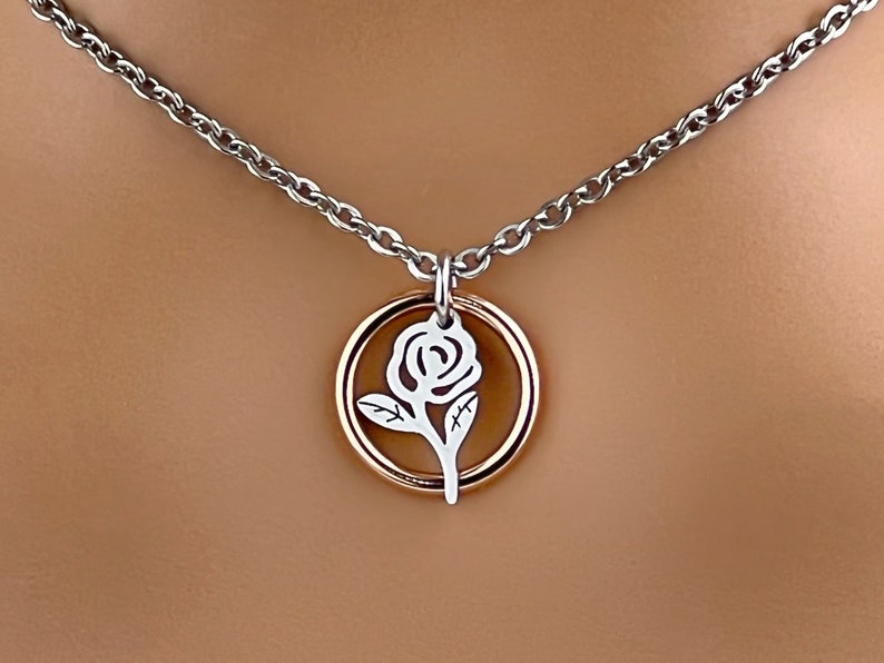 May include: Silver-tone necklace with a rose pendant. The pendant features a white rose design within a gold-tone circle. The necklace chain is a silver-tone cable chain.