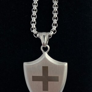 May include: A silver chain necklace with a silver shield pendant featuring a cross design.