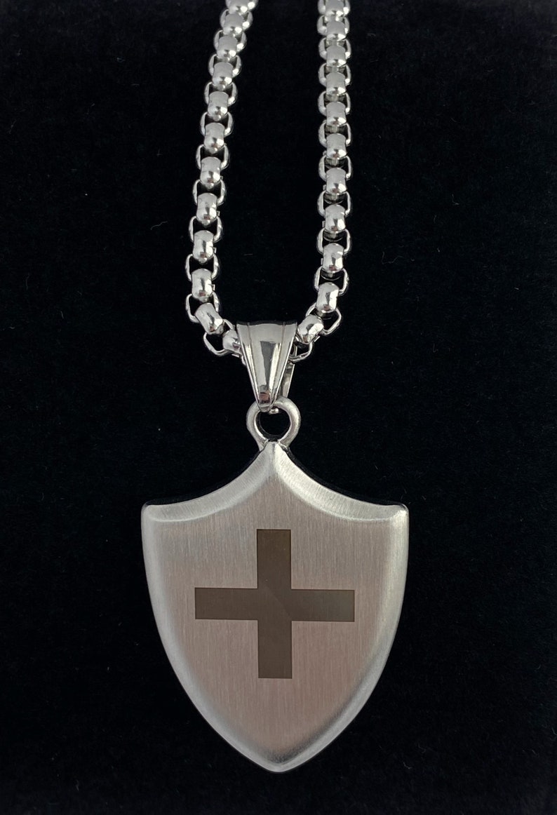 May include: A silver chain necklace with a silver shield pendant featuring a cross design.