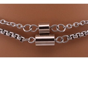 May include: A silver chain necklace with two layers and a silver cylindrical pendant.