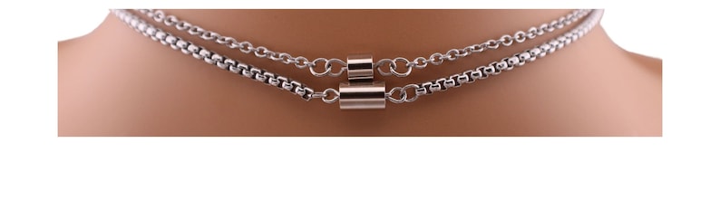 May include: A silver chain necklace with two layers and a silver cylindrical pendant.