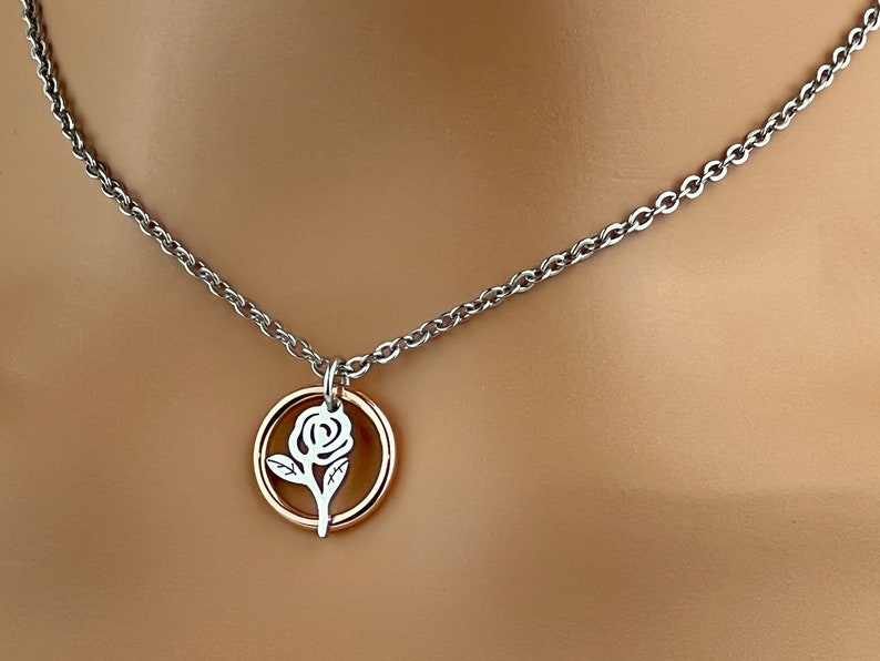 May include: A silver-toned necklace with a delicate rose pendant. The pendant features a rose design within a gold-colored circle. The chain is a simple, linked design, and the necklace is displayed against a neutral background.