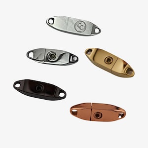 May include: An assortment of oval-shaped metal clasps in various finishes: silver, gold, bronze, and black. Each clasp features a central rivet and two small holes at either end for attachment. The silver clasp has a logo.