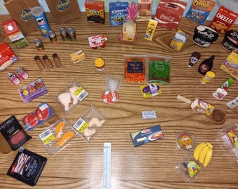 May include: A collection of miniature grocery items including branded food boxes, plastic-wrapped meat and produce, small cans, and bottles. The assortment features items like Coca-Cola, Ritz, Oreo, Cheez-It, and Breyers containers arranged on a surface.