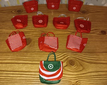 May include: A collection of ten miniature shopping bags and baskets. Three are red plastic baskets with white bullseye logos. Four are red fabric bags with white bullseye logos. Two are red fabric bags with white circular patterns. One is a green fabric bag.