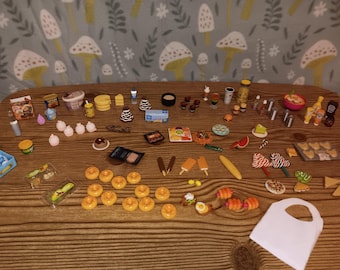 May include: A large collection of miniature food items and accessories, including tiny donuts, ice cream treats, packaged snacks, condiments, and small containers, arranged on a wooden surface with a mushroom-patterned fabric background.