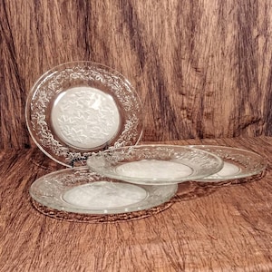May include: Three clear glass salad plates with a frosted floral design. The plates are stacked on top of each other.
