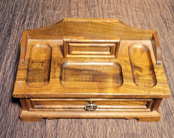 May include: Wooden desk organizer with a drawer and multiple compartments. The organizer is made of light brown wood and features a rectangular shape with a decorative handle on the drawer. The top has several recessed areas for storage.