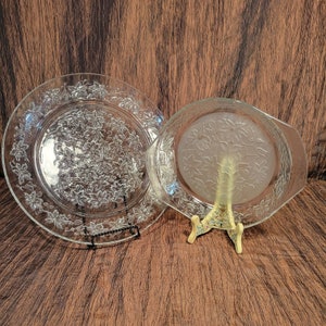 May include: Two clear glass serving dishes with a floral pattern. The dishes are on a wooden surface.