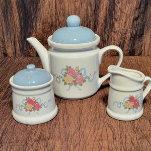 May include: A white tea set with a blue and floral design. The set includes a teapot, creamer, and sugar bowl.
