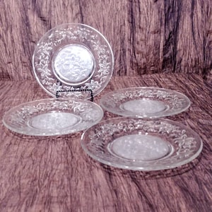 May include: Four clear glass dessert plates with a floral pattern. The plates are stacked on top of each other.