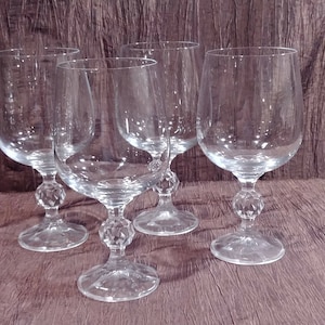 May include: Four clear glass wine glasses with a diamond-shaped pattern on the stem. The glasses are arranged in a semi-circle on a brown surface.