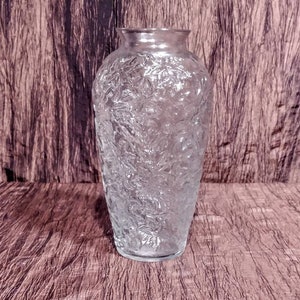 May include: A clear glass vase with a textured surface. The vase has a rounded body and a narrow opening.