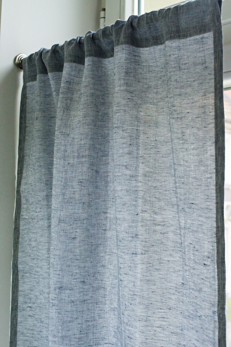 May include: A sheer linen curtain with a dark gray border. The curtain is hanging from a silver curtain rod.
