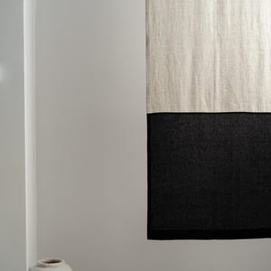 Puede incluir: Cortina de lino de dos tonos, con una secci&oacute;n superior en blanco roto natural y una secci&oacute;n inferior en negro. La cortina cuelga contra una pared blanca, con un jarr&oacute;n decorativo en la esquina.