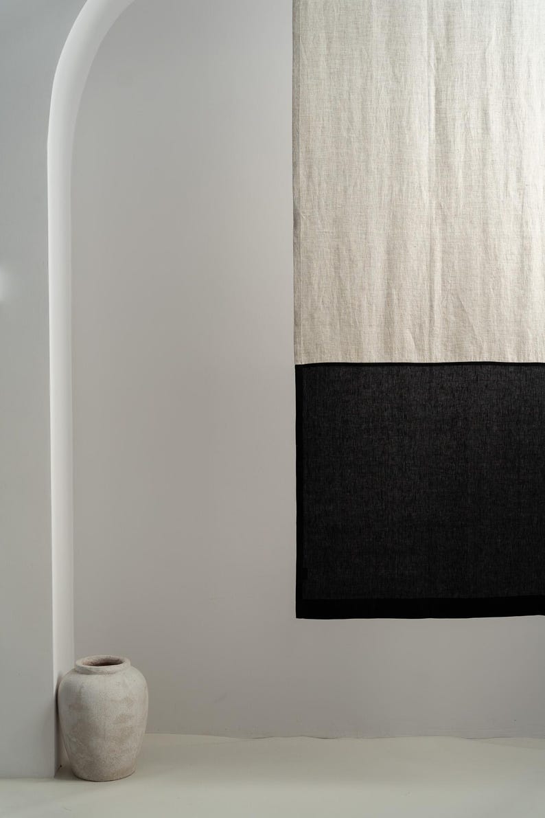 Puede incluir: Cortina de lino de dos tonos, con una secci&oacute;n superior en blanco roto natural y una secci&oacute;n inferior en negro. La cortina cuelga contra una pared blanca, con un jarr&oacute;n decorativo en la esquina.