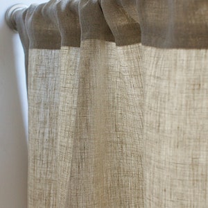 May include: Beige linen curtains hanging from a silver curtain pole. The curtains feature a textured weave and a darker beige band at the top. The fabric drapes in soft folds, creating a warm and inviting atmosphere.