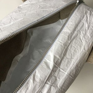 May include: A white zippered tote bag with a brown canvas handle. The bag is made of a crinkled, waterproof material.