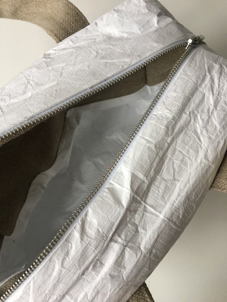 May include: A white zippered tote bag with a brown canvas handle. The bag is made of a crinkled, waterproof material.