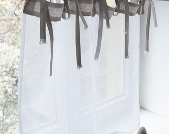 May include: Sheer white linen curtains with gray tie-top accents hanging from a silver rod. The curtains are in front of a window with a blurred outdoor view. Two small, gray bird figurines sit on the windowsill.