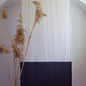 Puede incluir: Un tapiz de pared de lino de dos tonos. La secci&oacute;n superior es de color beige claro, la del medio es blanca y la inferior es gris oscuro. En primer plano, hierbas ornamentales secas, que a&ntilde;aden un elemento natural a la decoraci&oacute;n.