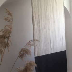 Puede incluir: Cortina rectangular de lino de dos tonos. La parte superior es de color beige claro y la inferior es negra. La cortina cuelga de una barra blanca, creando una est&eacute;tica minimalista. La tela parece ligeramente texturizada. Altura aproximada: 200 cm.