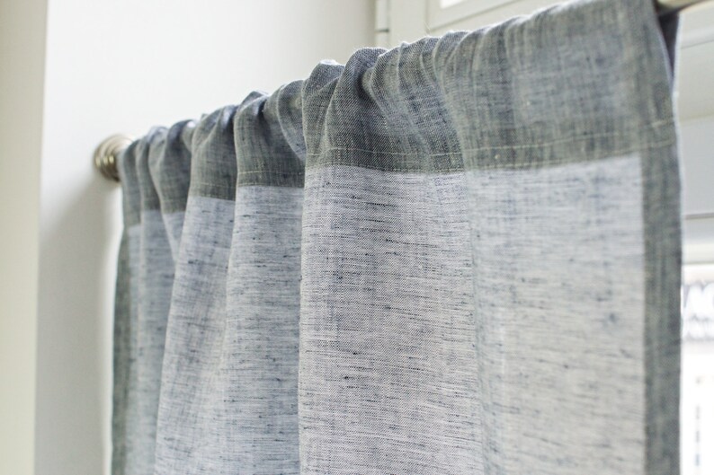 May include: A set of white linen curtains with a darker gray top border. The curtains are hung on a silver curtain rod.