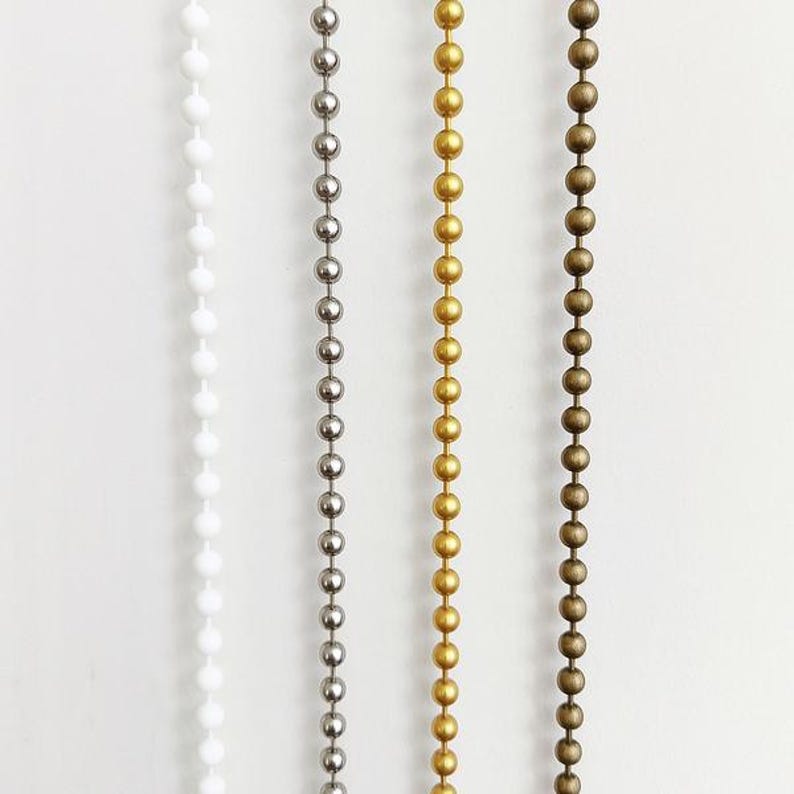 May include: Four beaded chains in white, silver, gold, and bronze colors. Each chain is composed of evenly spaced, round beads. The chains are vertically aligned against a white background, showcasing the variety of metallic and neutral tones.