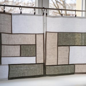Könnte beinhalten: Leinen-Patchwork-Vorhänge in Weiß-, Beige- und Olivgrüntönen mit dunkelbraunem Besatz. Die Vorhänge hängen an einer Metallstange mit Ringen. Eine dekorative Vogelfigur sitzt auf der Fensterbank.